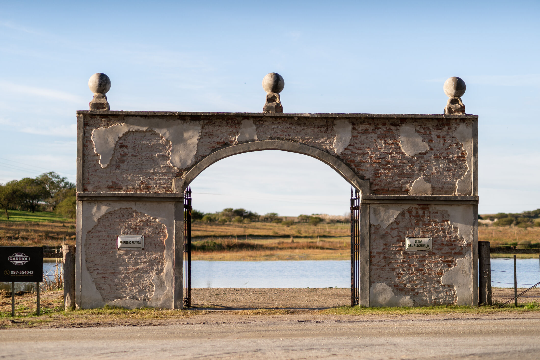 El portón histórico de Altos del Riachuelo, con la laguna detrás